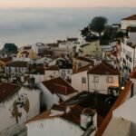Small town with aged houses on hill against sea with clouds in sunset