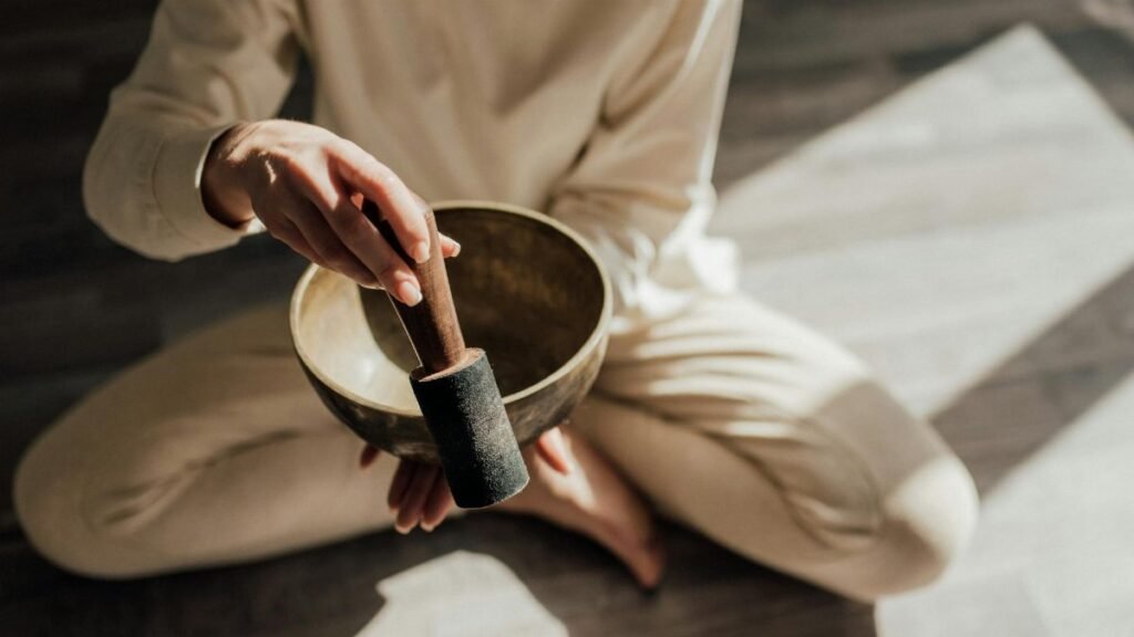 A person in meditation holding a Tibetan singing bowl in soft natural light.