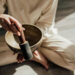 A person in meditation holding a Tibetan singing bowl in soft natural light.