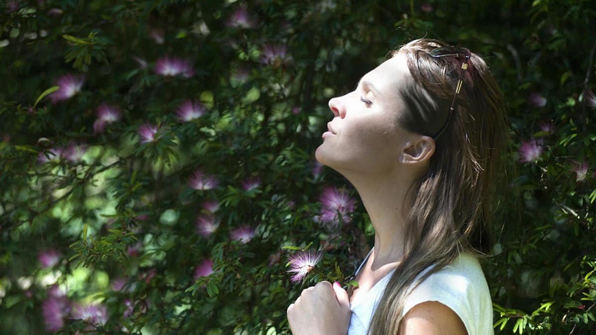 A woman enjoying a serene moment in a sunlit garden, surrounded by vibrant flowers.