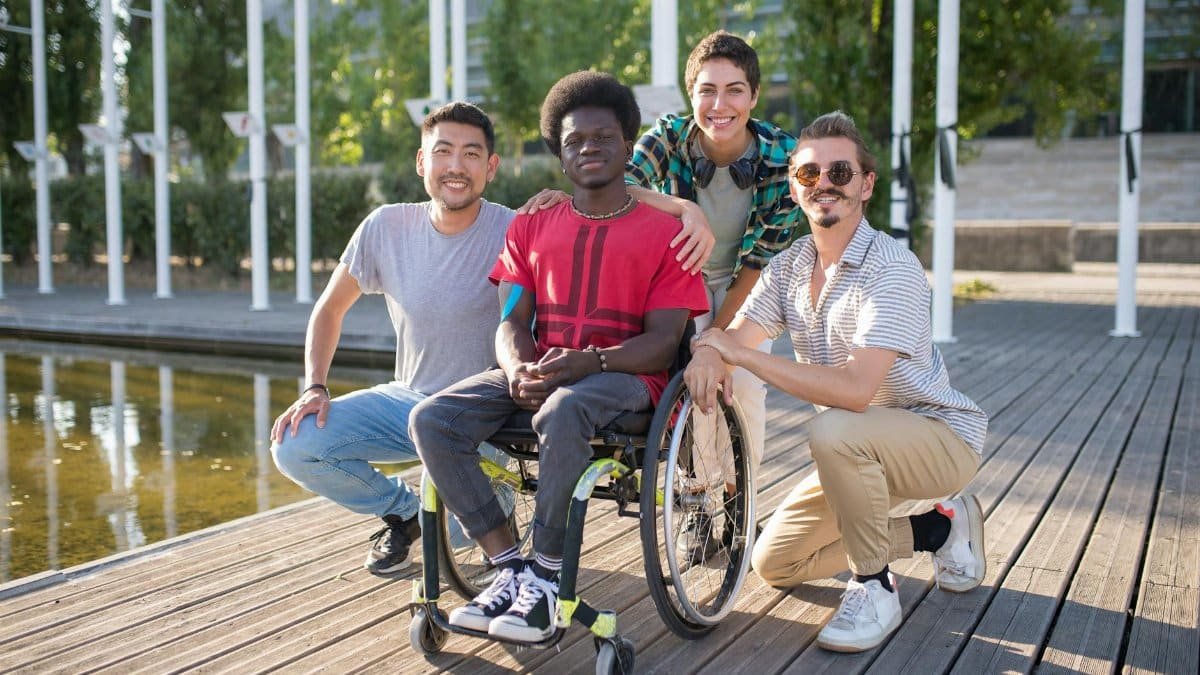 Group of diverse friends, including a person in a wheelchair, enjoying a sunny day at the park.
