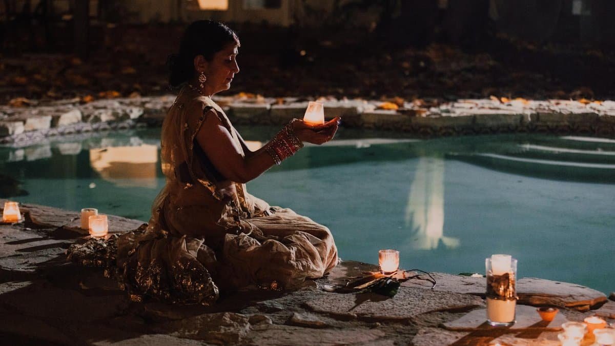An Indian woman in traditional attire celebrating Diwali with candles by the poolside at night.