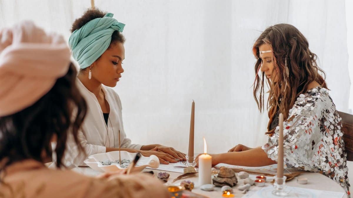 Three women engaging in a spiritual meditation session indoors with candles and crystals.