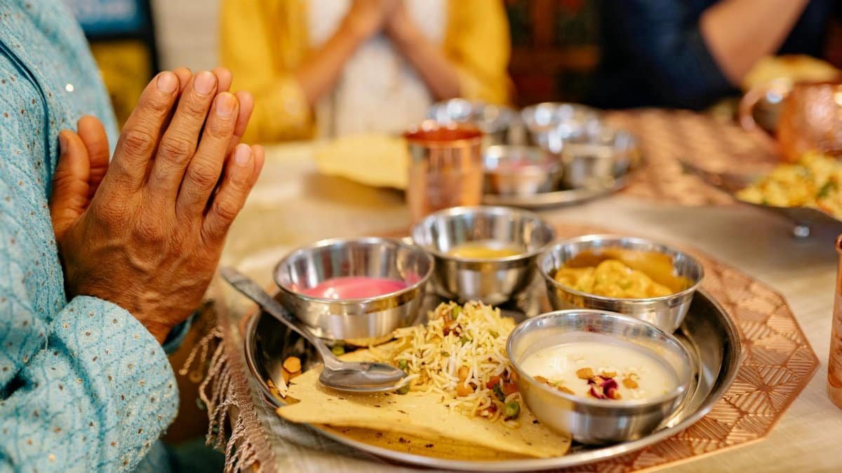 Close-up of a traditional Indian meal with hands in prayer, reflecting cultural dining rituals.