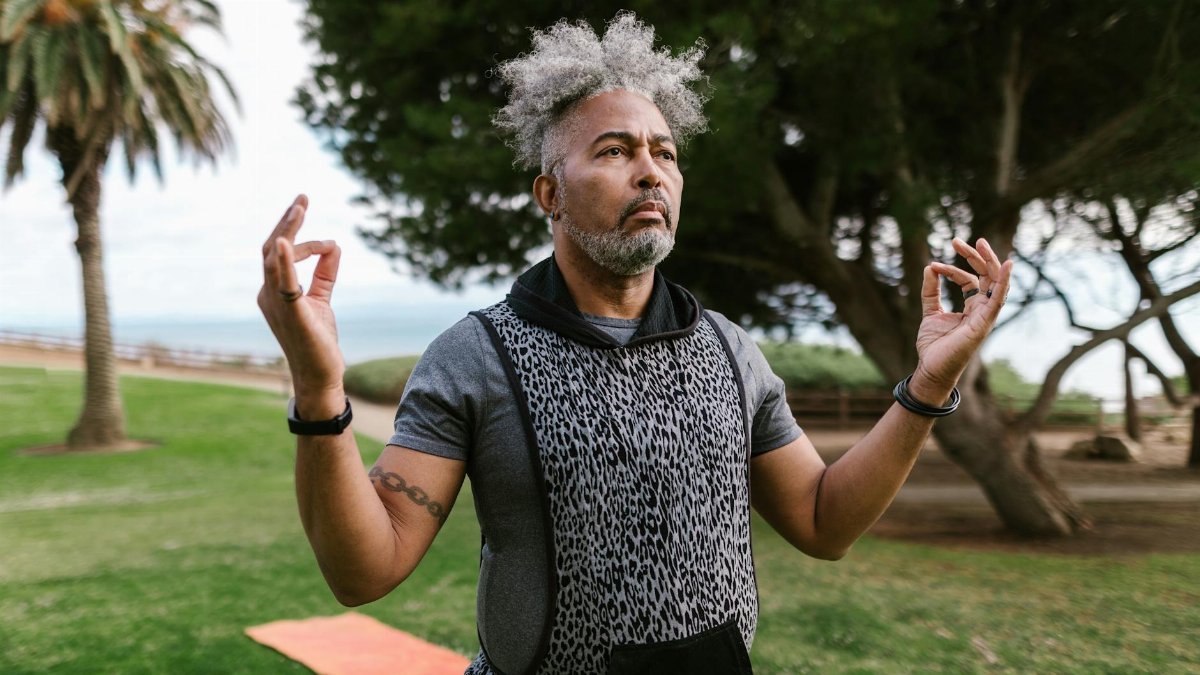 Serene senior man practicing meditation and wellness exercises in a lush green park.