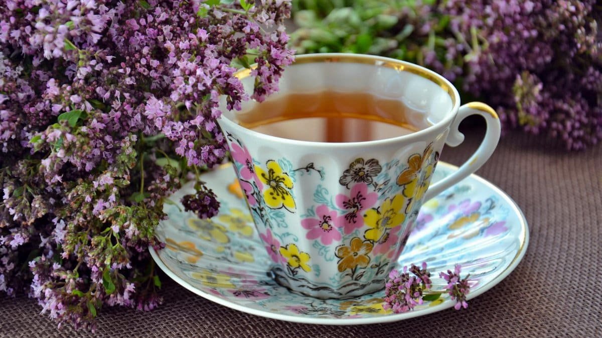 A beautiful porcelain teacup with floral patterns, filled with herbal tea, surrounded by lavender flowers.