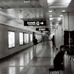 A black and white photo of a subway station corridor with signs and people walking.