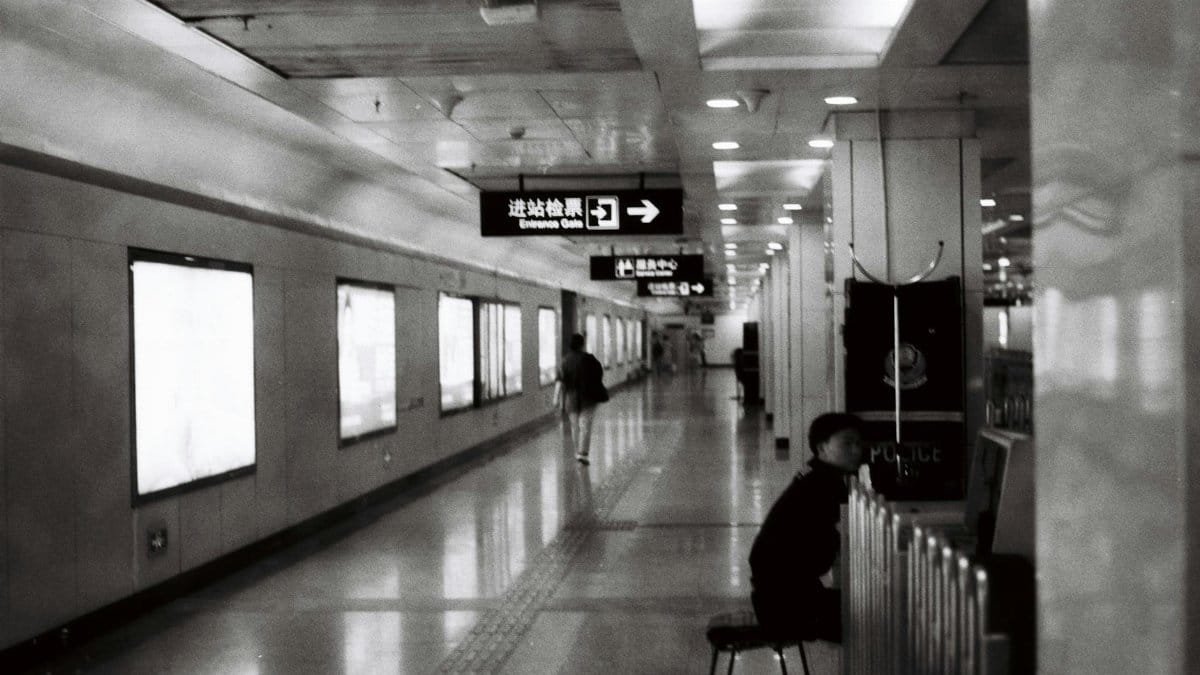 A black and white photo of a subway station corridor with signs and people walking.