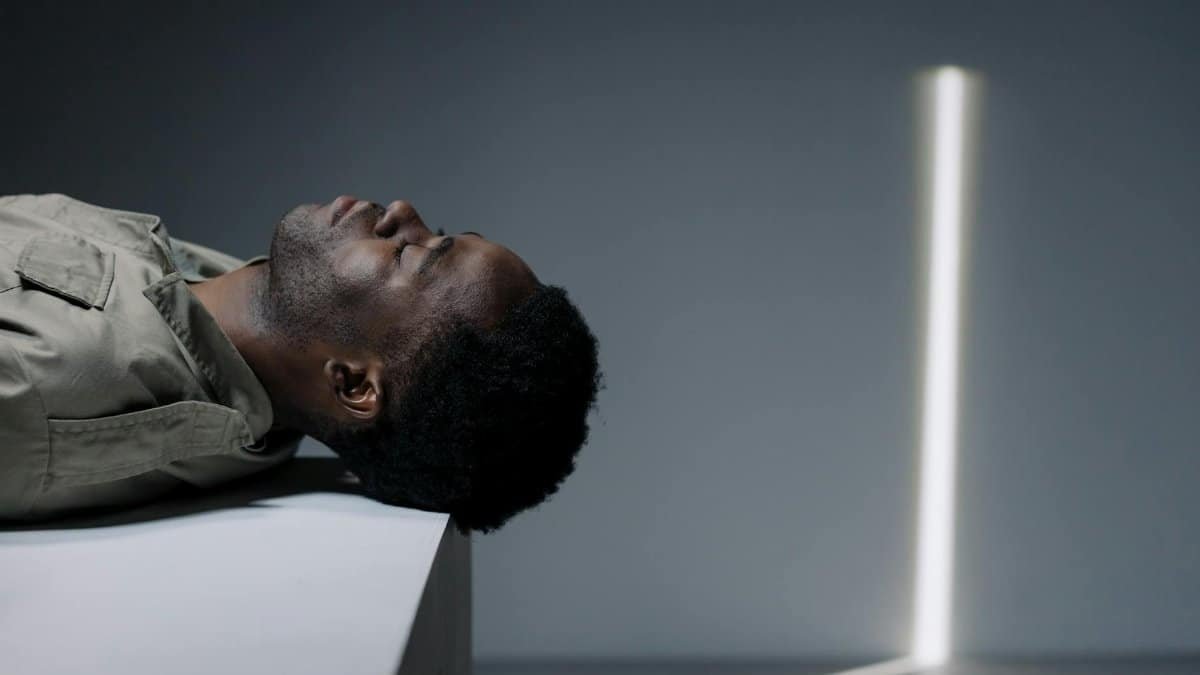 A black man with eyes closed lying down in a studio shoot with unique light and shadow effects.