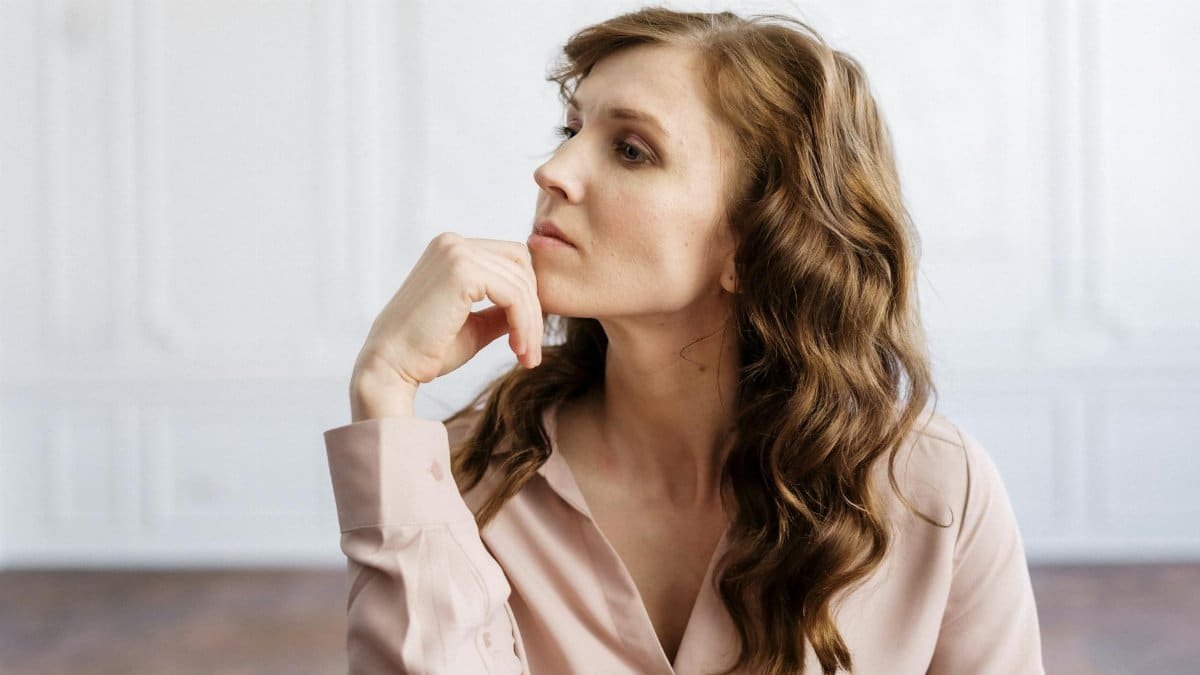 A thoughtful woman with curly hair sits indoors, reflecting deeply in a serene setting.