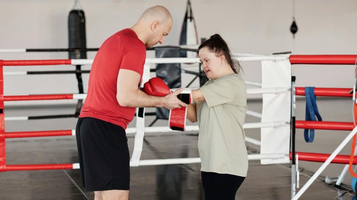 Boxing trainer helping young woman with Down syndrome during a training session in a gym.