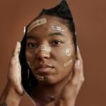 African American woman with Band-Aids looks into a shattered mirror, reflecting self-acceptance.