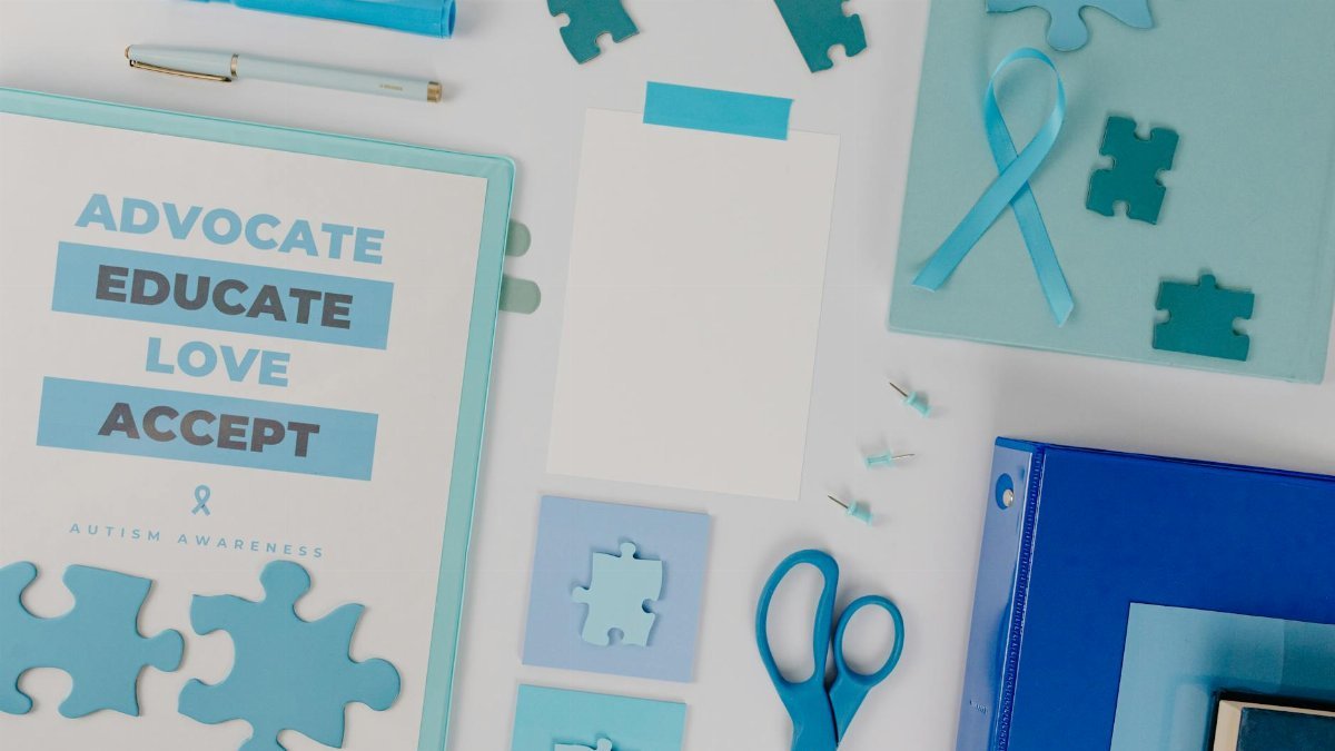 Flat lay of autism awareness materials with blue puzzle pieces and ribbon, promoting acceptance.