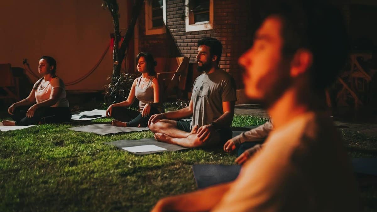 A group of people practicing yoga meditation outdoors at dusk in a peaceful garden setting.