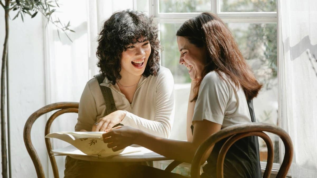 Laughing multiracial female colleagues wearing uniform flipping pages of papers while discussing work together