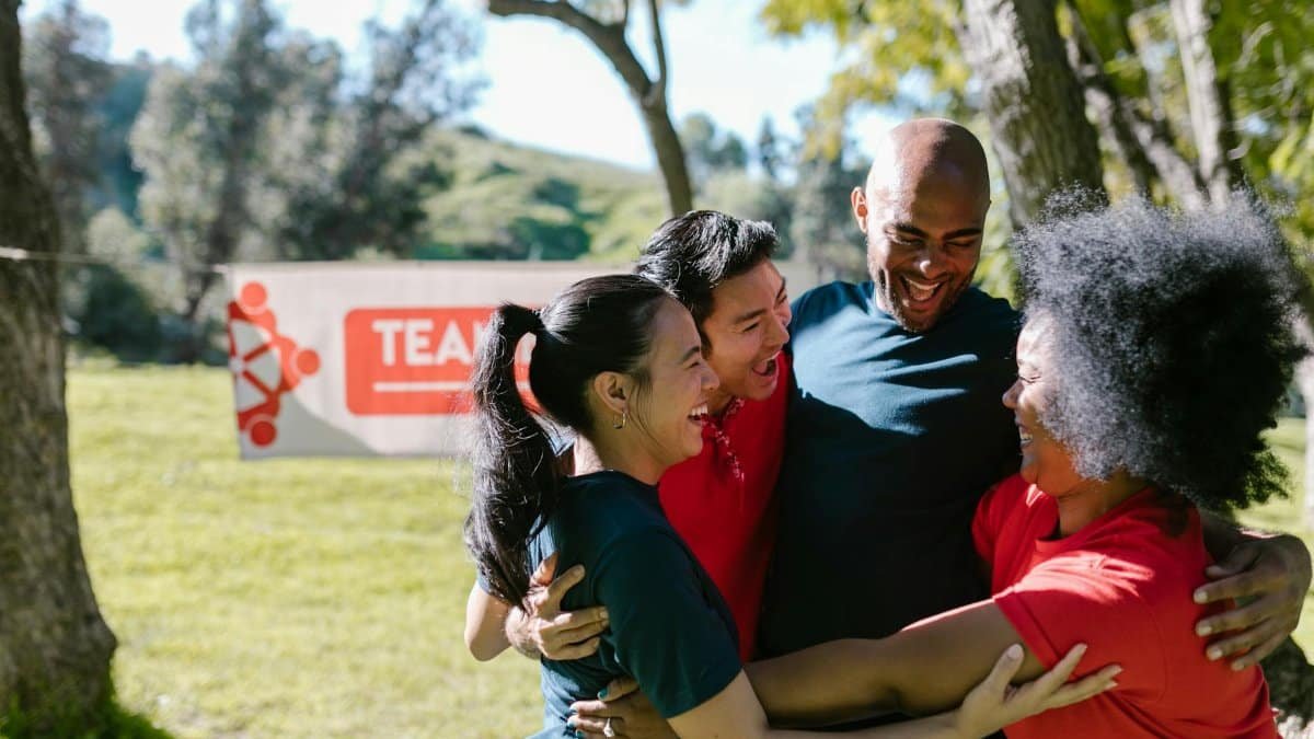 A joyful group of friends embracing in a team building event outdoors.