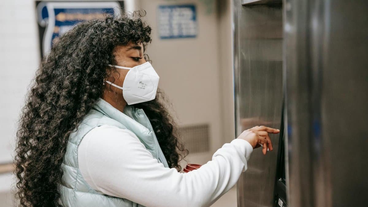 Woman wearing face mask uses ATM in an indoor setting, reflecting pandemic safety measures.