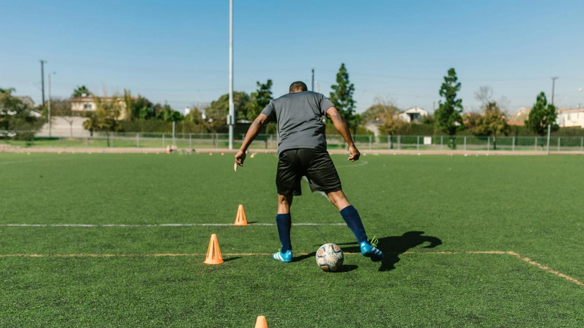A soccer player practicing drills on a sunny day on an outdoor field.