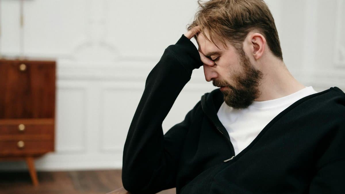 A man sits pensively with his hand on his face, capturing a moment of introspection and stress.