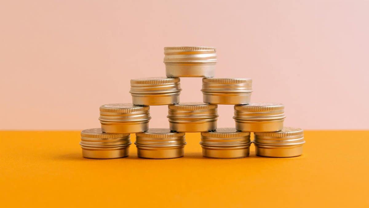 A geometric stack of metallic caps on an orange surface with a soft pink background.