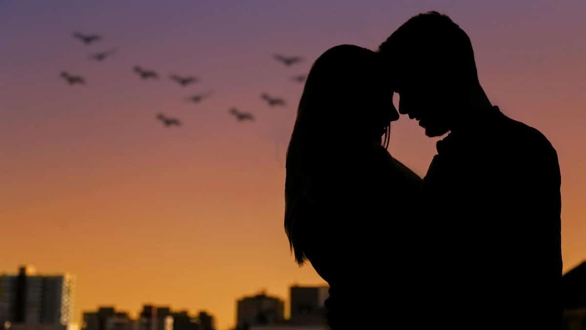 Silhouette of a couple embracing at sunset in an urban setting, evoking romance.