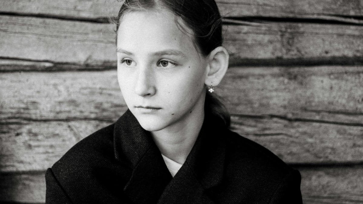 Thoughtful black and white portrait of a young girl in front of wooden wall.