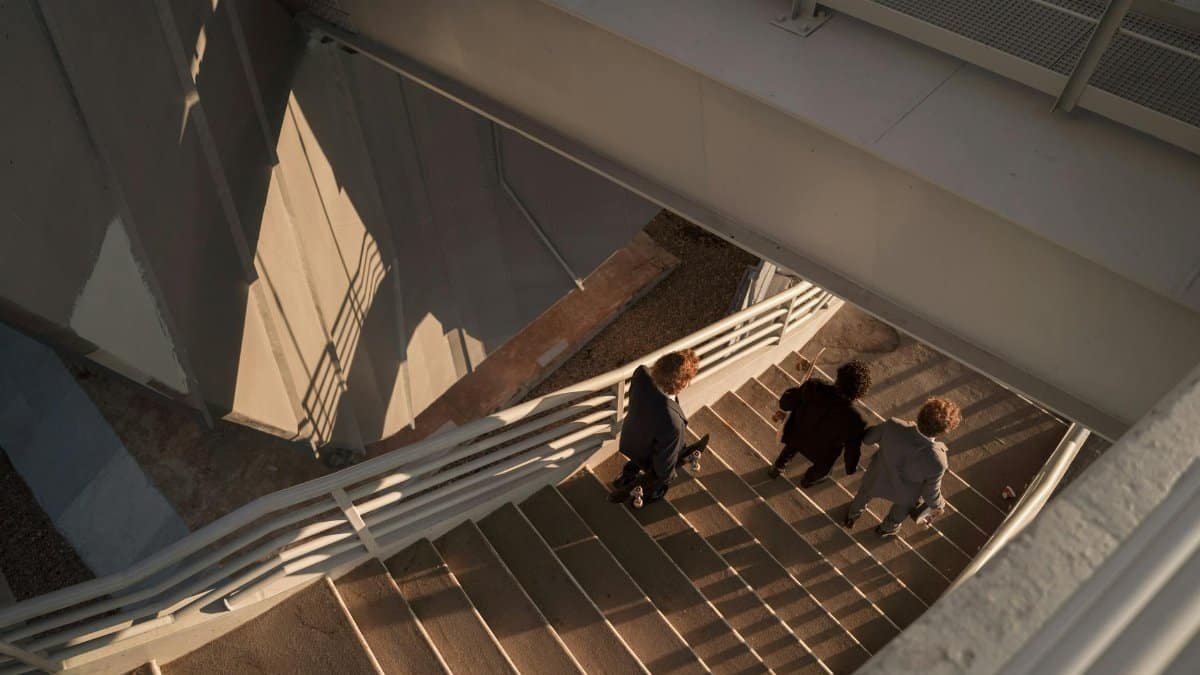 Three men in suits walk down stairs in modern industrial setting captured from above.