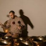 A man using Tibetan singing bowls for healing and relaxation in a serene indoor setting.