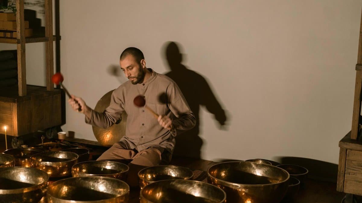 A man using Tibetan singing bowls for healing and relaxation in a serene indoor setting.