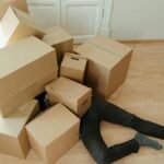 A person overwhelmed by cardboard boxes during a home move, symbolizing stress and relocation.