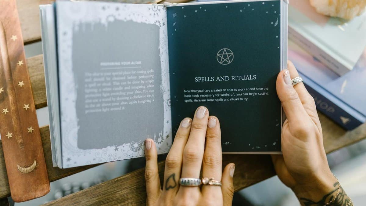 Close-up of hands holding an open book about spells and rituals, featuring a pentagram symbol.