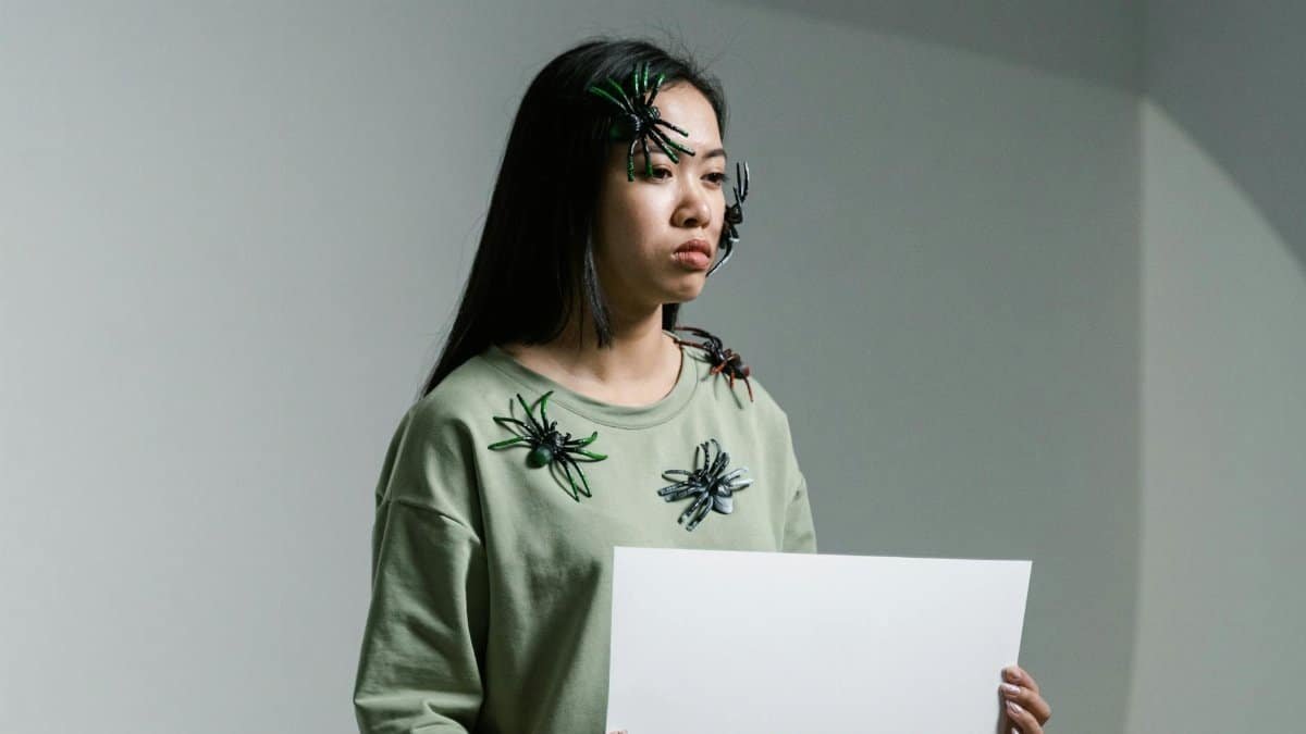 Woman holding arachnophobia sign with toy spiders on face, expressing fear.