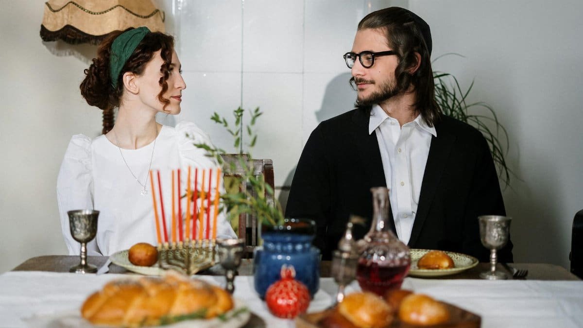 Couple enjoying a traditional Jewish meal with challah bread and menorah.