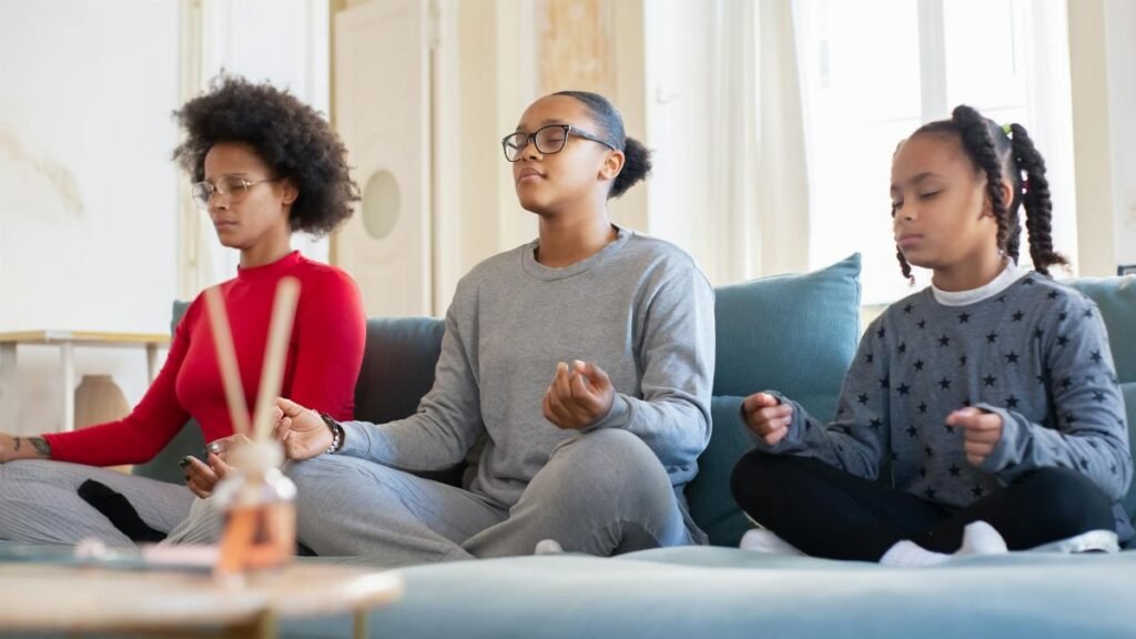 A family of three meditates together on a living room couch, promoting mindfulness.