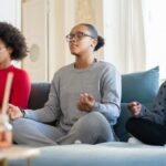 A family of three meditates together on a living room couch, promoting mindfulness.