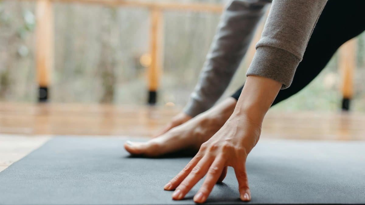 A person stretches their hand and foot on a yoga mat indoors, focusing on wellness.