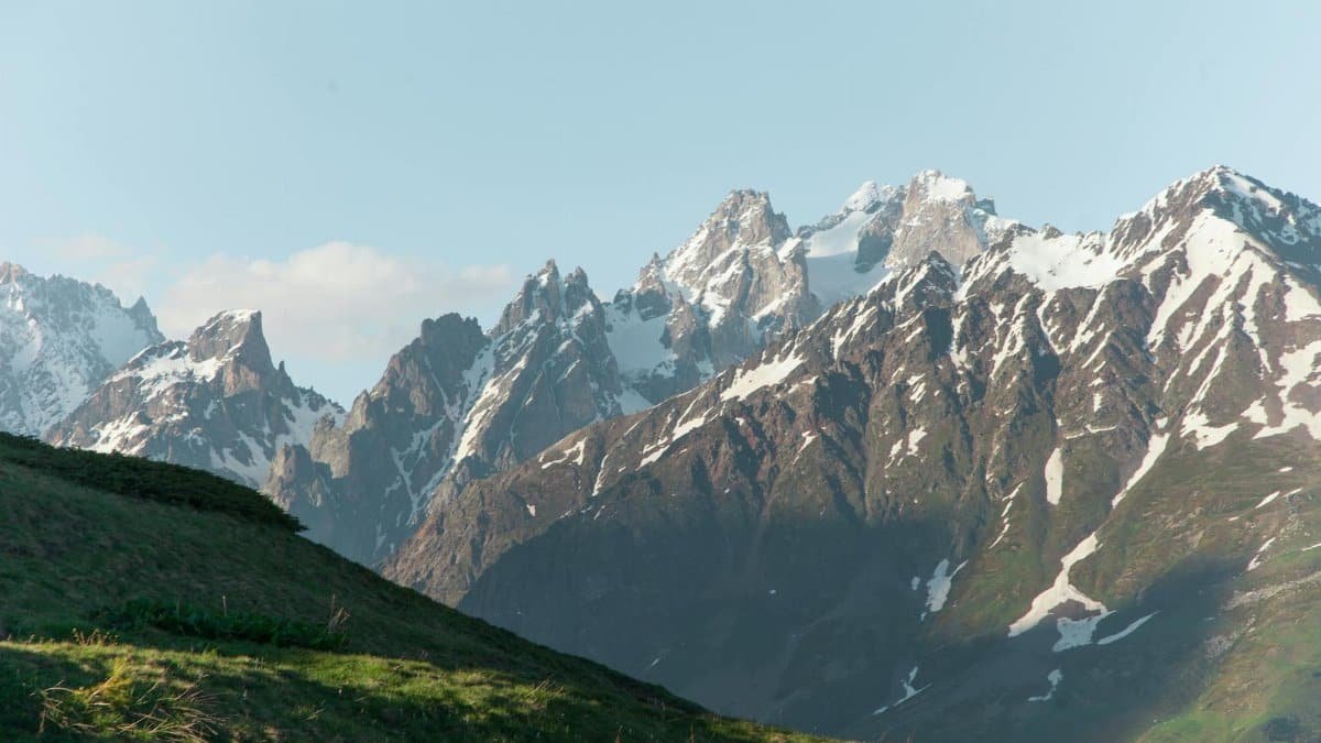 Dramatic snow-capped mountains towering over a lush grass field, capturing nature's majesty.