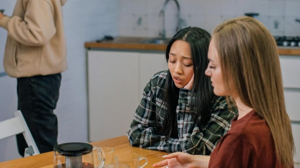 Two women in conversation at a table, offering emotional support over tea in a cozy indoor setting.