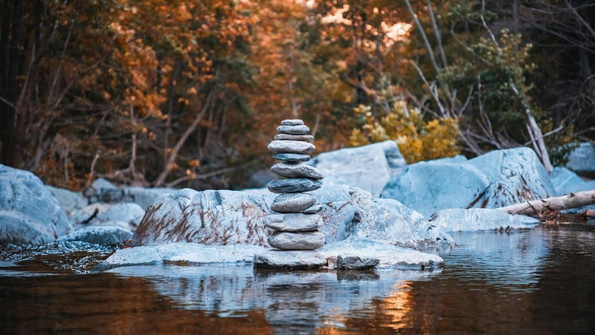 Calm forest scene with balanced stones on a riverbed, showcasing vibrant autumn foliage.