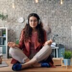 Young woman meditating with headphones in a modern office setting, practicing mindfulness.