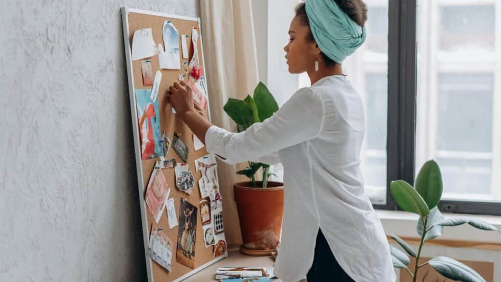 Woman in white shirt arranging a vision board in a modern apartment.