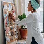 Woman in white shirt arranging a vision board in a modern apartment.