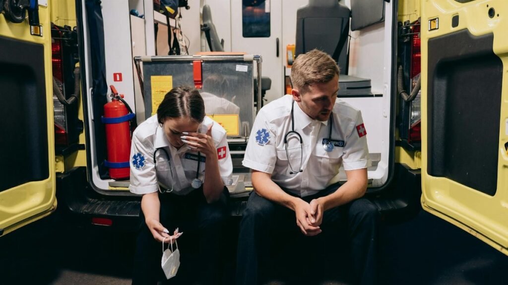 Two paramedics sitting tired at the back of an ambulance, reflecting the stress of emergency services.