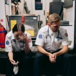 Two paramedics sitting tired at the back of an ambulance, reflecting the stress of emergency services.