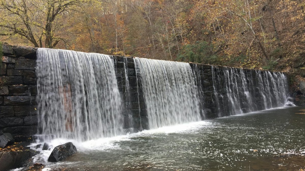 Beautiful waterfall cascading over a stone wall surrounded by fall foliage in Lynchburg, Virginia.