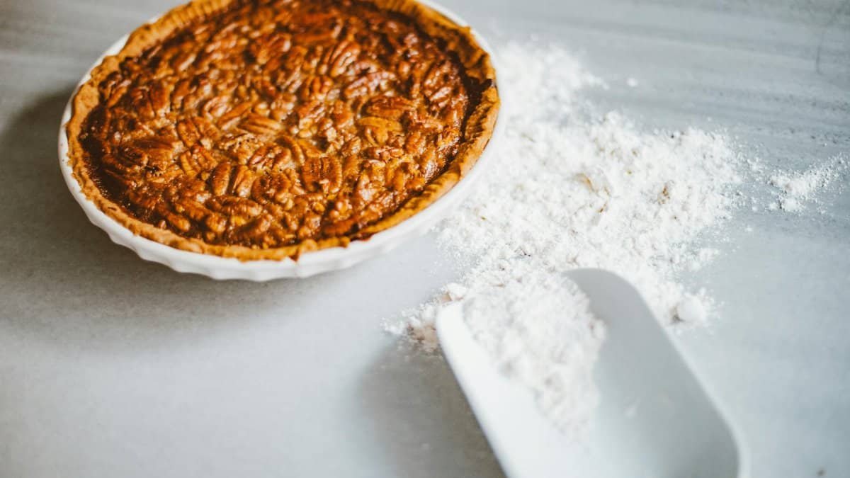 Close-up of a freshly baked pecan pie with scattered flour on a marble surface, inviting dessert lovers.