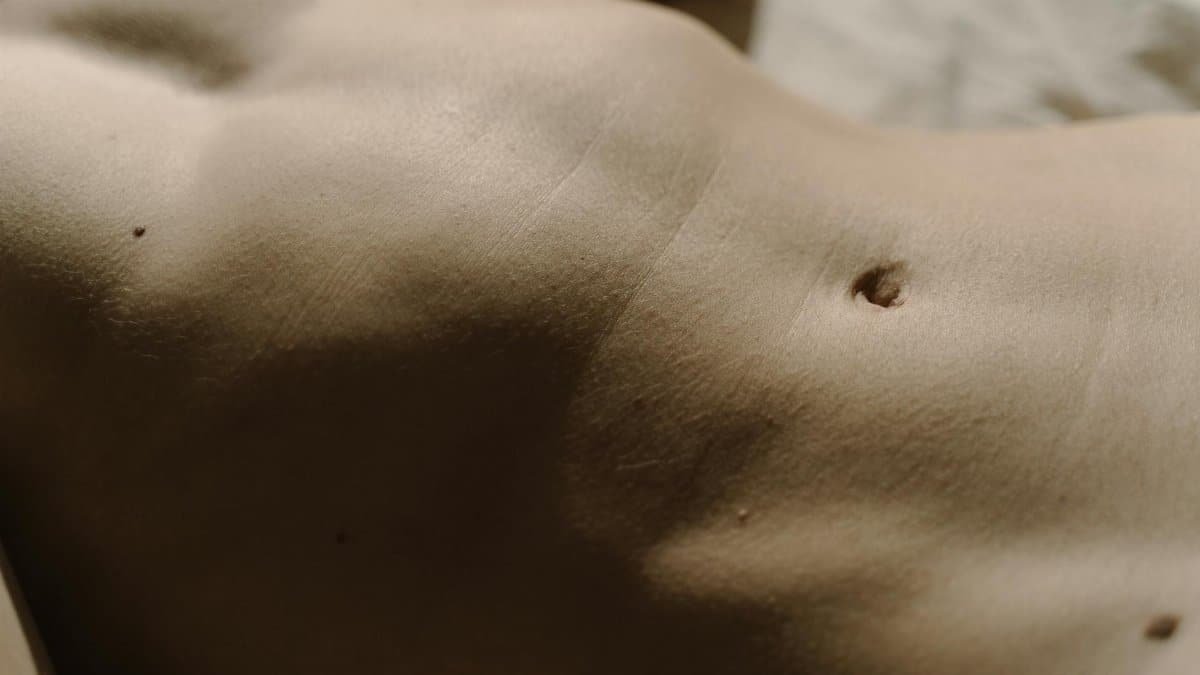 Detailed close-up of human skin featuring belly button, texture, and moles under natural light.