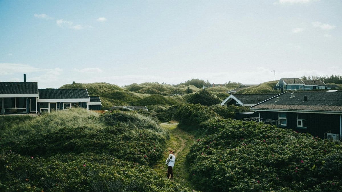 Explore a picturesque Nordic coastal village with lush green dunes and traditional houses.