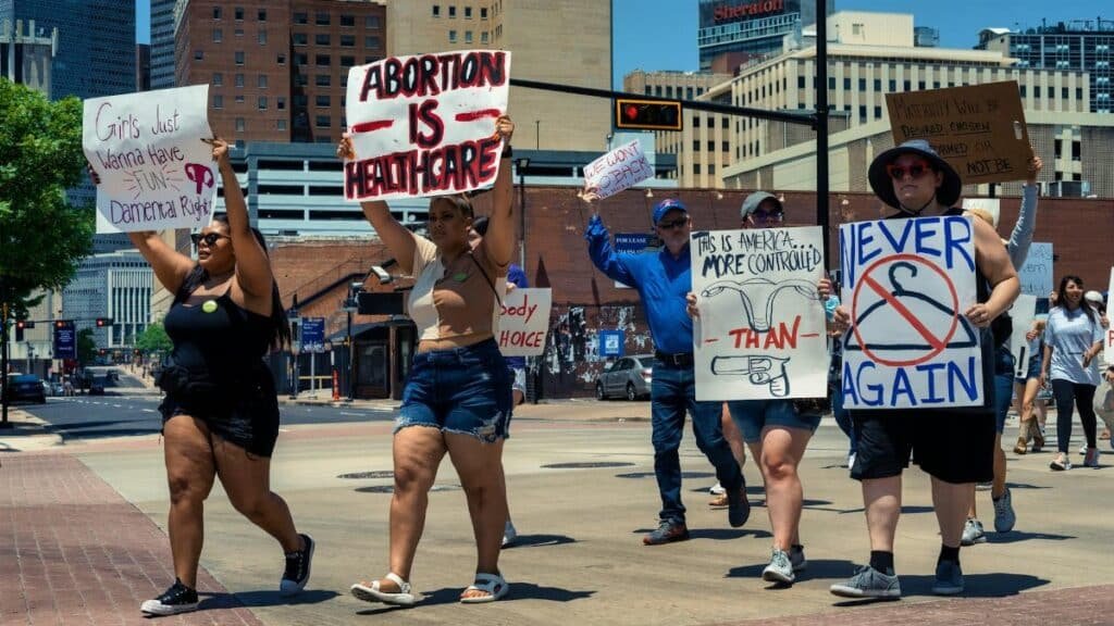 Group of diverse activists marching with signs in a city street advocating for women's rights and healthcare.
