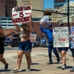 Group of diverse activists marching with signs in a city street advocating for women's rights and healthcare.